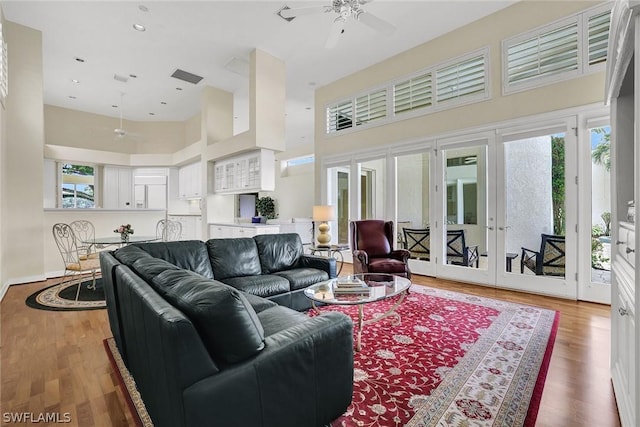 living room featuring ceiling fan, a towering ceiling, and wood-type flooring