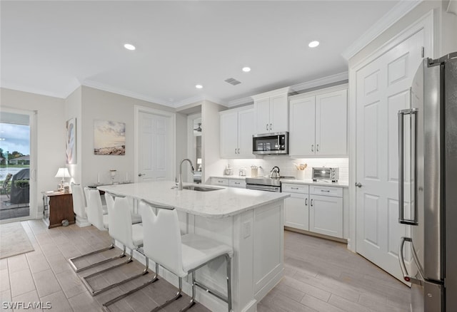 kitchen featuring a center island with sink, appliances with stainless steel finishes, light stone counters, sink, and white cabinetry