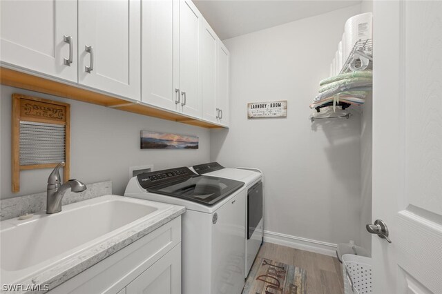 laundry area featuring sink, wood-type flooring, washer and clothes dryer, and cabinets