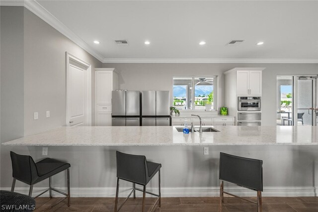 kitchen featuring light stone counters, a kitchen bar, appliances with stainless steel finishes, and white cabinetry