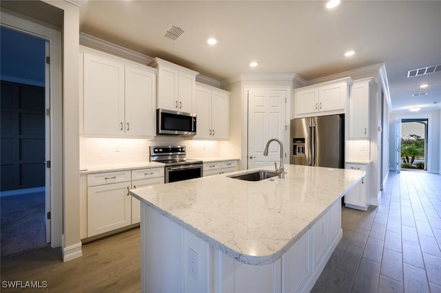 kitchen with appliances with stainless steel finishes, an island with sink, sink, white cabinets, and crown molding