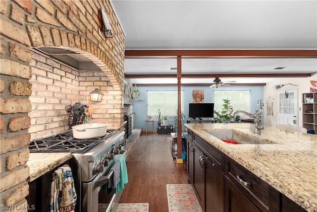 kitchen featuring sink, stainless steel stove, dark brown cabinets, light stone countertops, and a brick fireplace