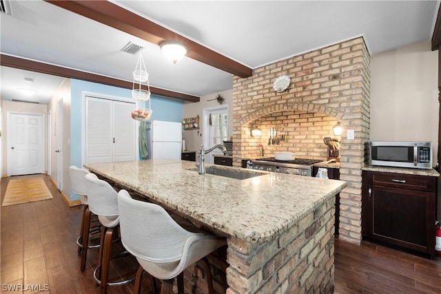 kitchen with sink, white fridge, range, light stone counters, and a center island with sink