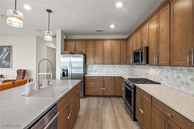 kitchen with brown cabinets, stainless steel appliances, visible vents, hanging light fixtures, and a sink