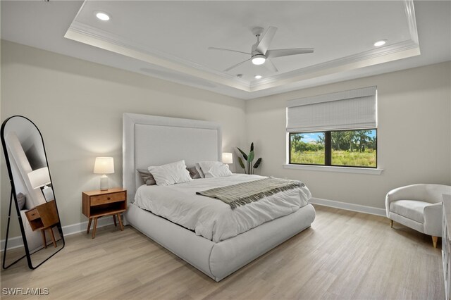 bedroom with light wood-style floors, a tray ceiling, crown molding, and baseboards