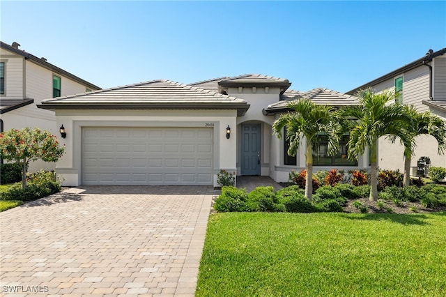 view of front of property featuring a garage, a tiled roof, decorative driveway, stucco siding, and a front yard