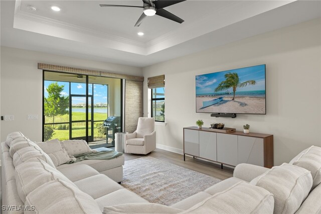 living room with ceiling fan, hardwood / wood-style flooring, a raised ceiling, and ornamental molding