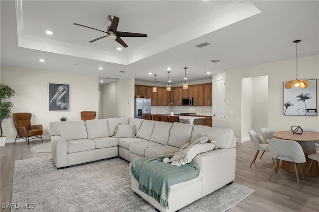 living area with a tray ceiling, light wood-type flooring, recessed lighting, and crown molding