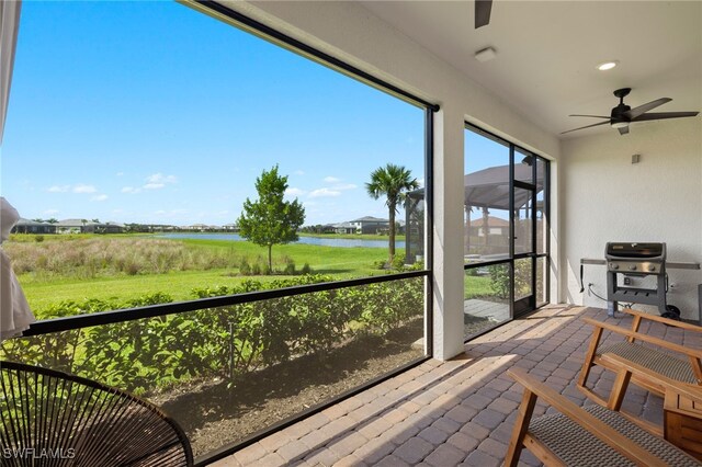 sunroom / solarium with a ceiling fan and a water view