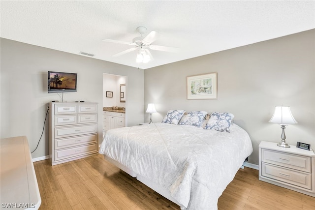 bedroom featuring a textured ceiling, ceiling fan, light hardwood / wood-style flooring, and ensuite bath