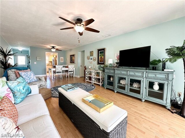 living room with a textured ceiling, ceiling fan, and light hardwood / wood-style floors