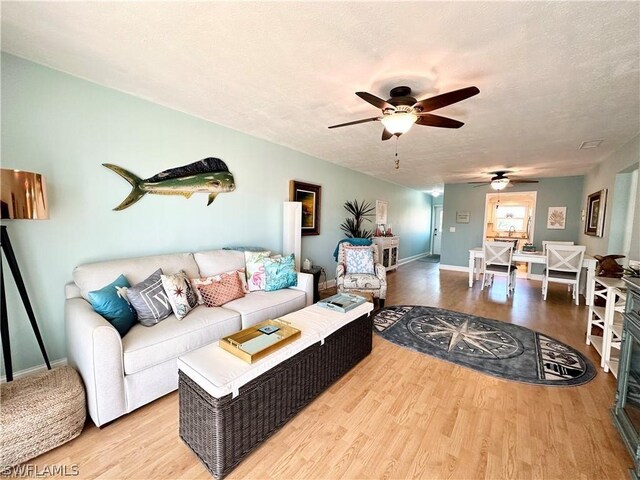 living room with light hardwood / wood-style floors, a textured ceiling, and ceiling fan