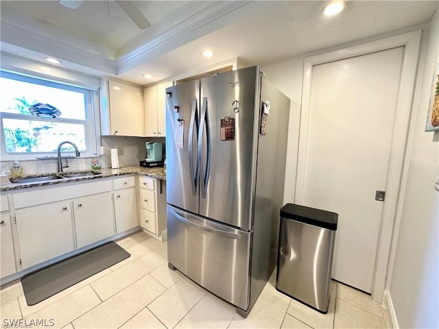 kitchen featuring white cabinetry, sink, light stone countertops, stainless steel refrigerator, and light tile patterned floors