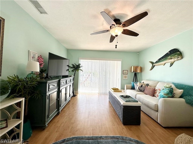 living room with ceiling fan, a textured ceiling, and light hardwood / wood-style flooring