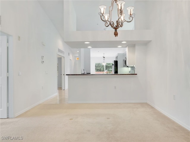 unfurnished living room with light colored carpet, a high ceiling, and a chandelier