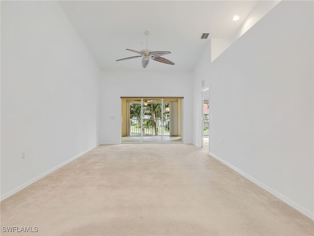 empty room featuring light carpet, a ceiling fan, a towering ceiling, visible vents, and baseboards