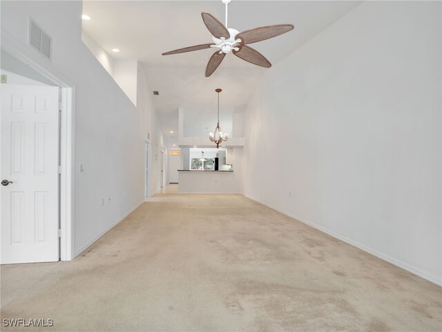 unfurnished living room with ceiling fan with notable chandelier, light colored carpet, and high vaulted ceiling