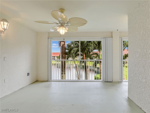 spare room featuring concrete flooring, a textured wall, ceiling fan, and a water view