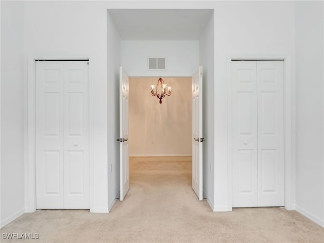 hallway featuring light carpet, baseboards, visible vents, and an inviting chandelier