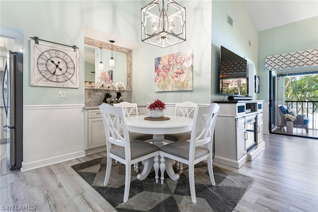 dining space featuring light wood-type flooring, high vaulted ceiling, and an inviting chandelier