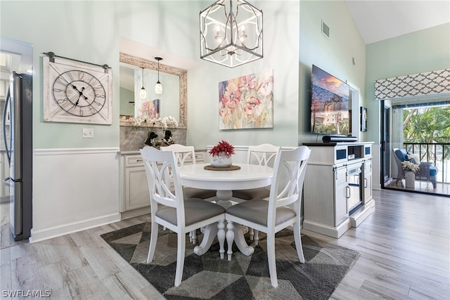 dining area featuring high vaulted ceiling, light hardwood / wood-style floors, and a notable chandelier