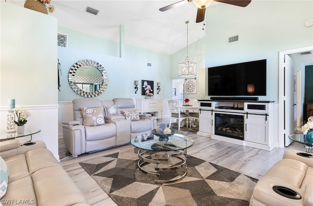 living room with high vaulted ceiling, ceiling fan with notable chandelier, and light wood-type flooring