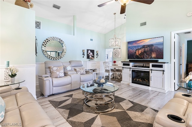 living room featuring high vaulted ceiling, ceiling fan with notable chandelier, and light wood-type flooring