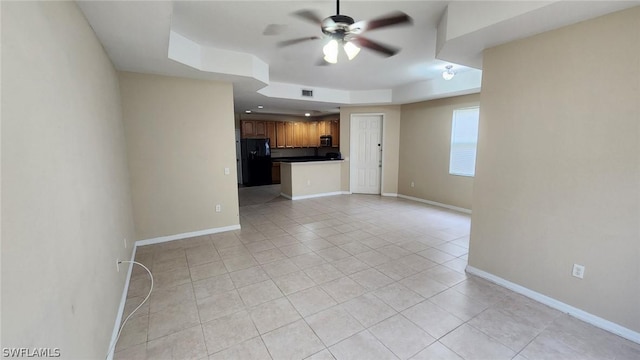 unfurnished living room featuring a tray ceiling, ceiling fan, and light tile patterned flooring