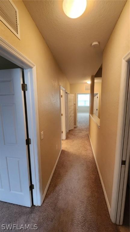 hallway with a textured ceiling and light colored carpet