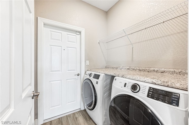 clothes washing area with washing machine and clothes dryer and light wood-type flooring