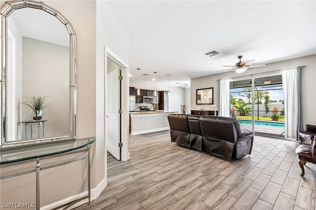 living room with ceiling fan, sink, and light wood-type flooring