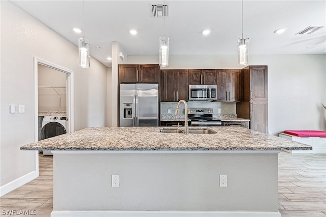 kitchen featuring washer / dryer, sink, a center island with sink, appliances with stainless steel finishes, and light stone countertops