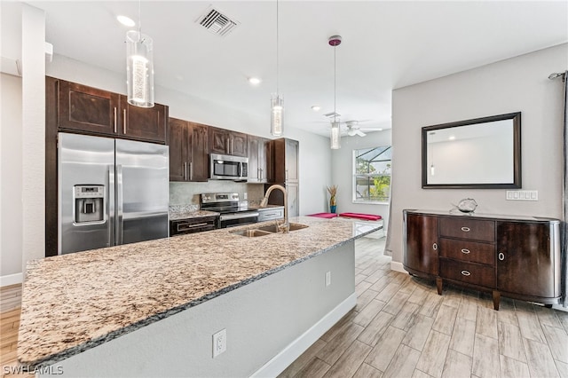 kitchen featuring stainless steel appliances, hanging light fixtures, dark brown cabinets, and light stone counters