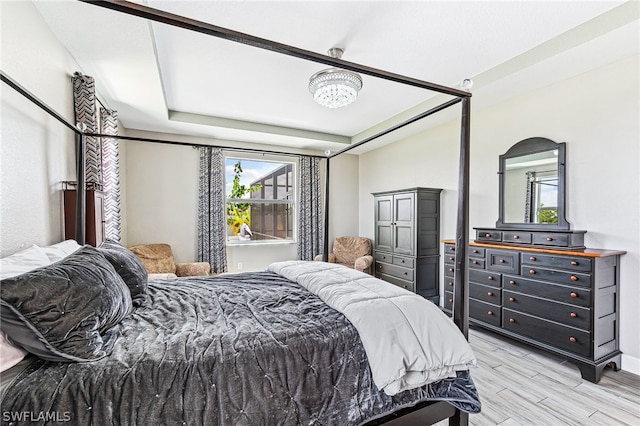 bedroom with a tray ceiling and light wood-type flooring