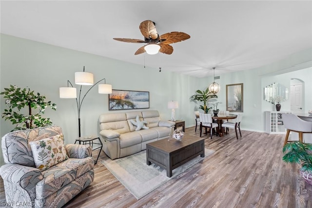 living room with ceiling fan with notable chandelier and light hardwood / wood-style floors