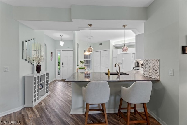 kitchen featuring kitchen peninsula, a kitchen bar, sink, white refrigerator with ice dispenser, and hanging light fixtures