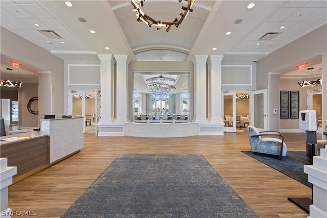 interior space featuring a towering ceiling, light wood-type flooring, decorative columns, and an inviting chandelier