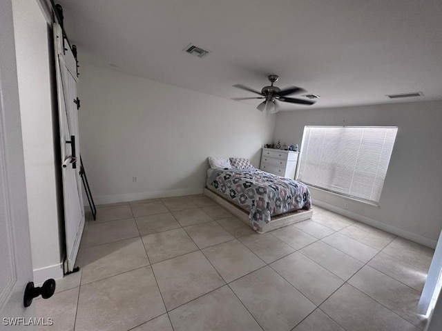 unfurnished bedroom with a barn door, ceiling fan, and light tile patterned floors