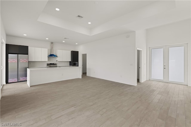 unfurnished living room featuring a raised ceiling, french doors, light hardwood / wood-style flooring, and sink