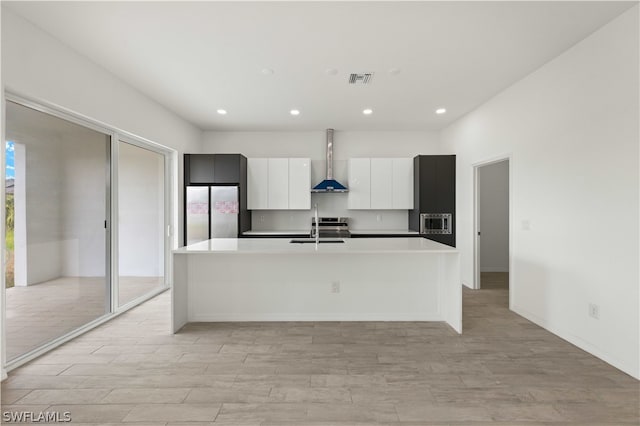 kitchen featuring appliances with stainless steel finishes, wall chimney range hood, sink, light hardwood / wood-style floors, and an island with sink