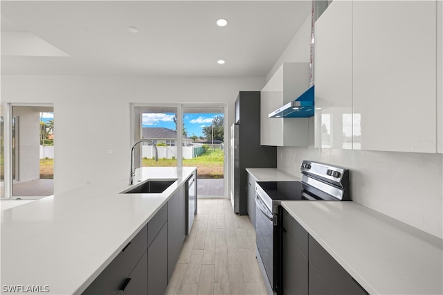 kitchen with white cabinetry, wall chimney range hood, electric range oven, light hardwood / wood-style floors, and sink