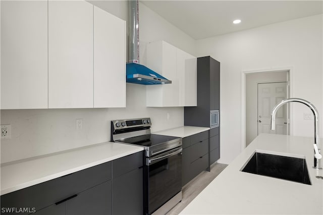 kitchen with white cabinetry, light wood-type flooring, wall chimney range hood, stainless steel range with electric stovetop, and sink