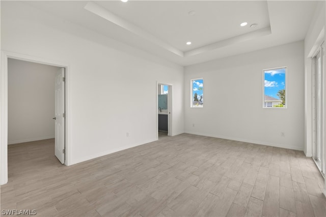 empty room with light hardwood / wood-style floors and a tray ceiling