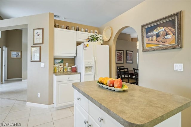 kitchen with light tile patterned flooring, white fridge with ice dispenser, white cabinets, and a kitchen island