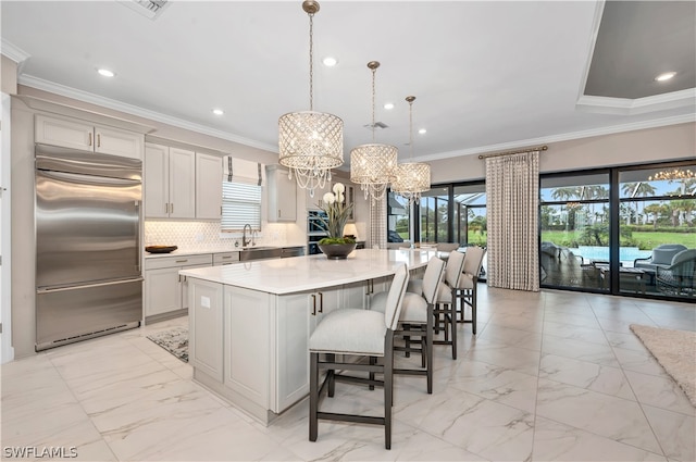 kitchen featuring a notable chandelier, hanging light fixtures, decorative backsplash, built in refrigerator, and a center island