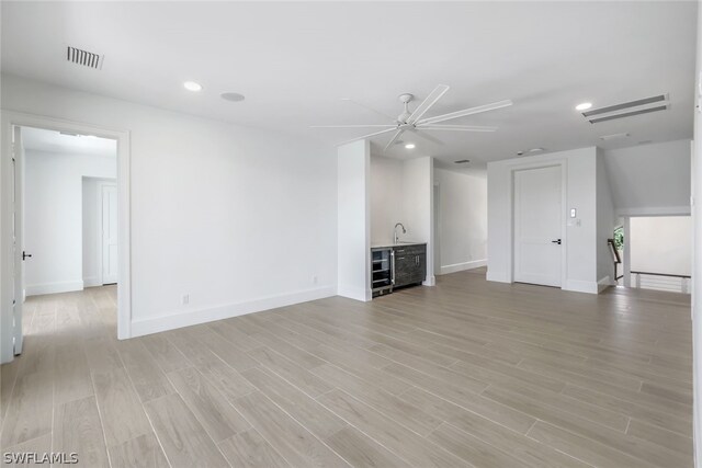 unfurnished living room with sink, light wood-type flooring, ceiling fan, and wine cooler