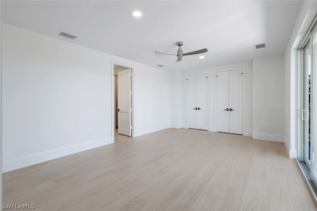 unfurnished bedroom featuring baseboards, multiple closets, visible vents, and light wood-style floors