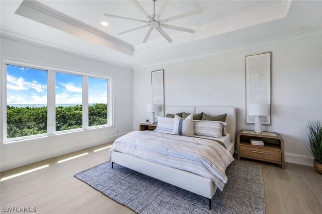 bedroom with wood-type flooring, ceiling fan, a raised ceiling, and ornamental molding