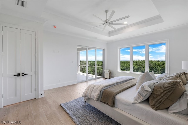 bedroom featuring a raised ceiling, light hardwood / wood-style flooring, access to exterior, and ceiling fan