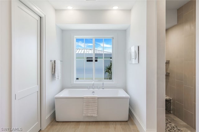 bathroom with wood finished floors, walk in shower, a freestanding tub, and baseboards